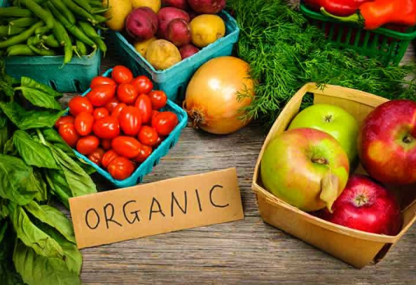 Alimentos frescos em uma feira comparando comida orgânica vs. convencional, com frutas e verduras coloridas.